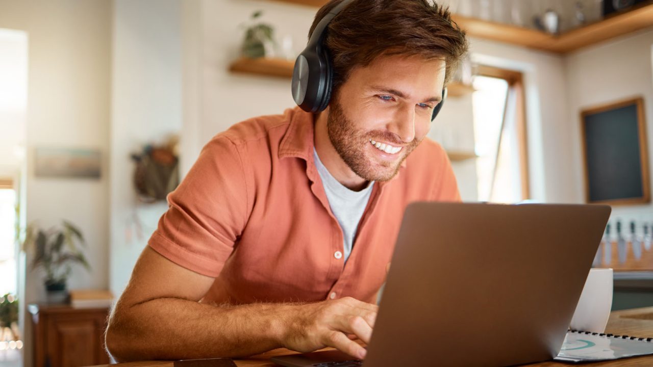 Headphones, laptop and remote work, happy man in kitchen on vide