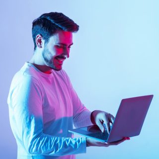 Work and play online. Happy guy holding laptop and typing