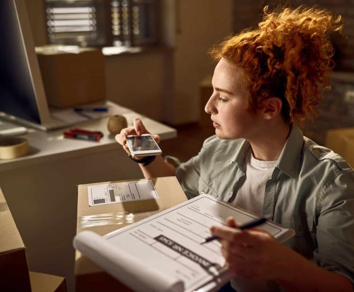 Yung woman preparing packages for delivery and scanning bar code