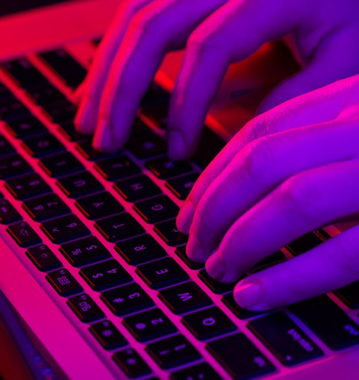 A man uses a laptop, close up, male hands in neon lighting.